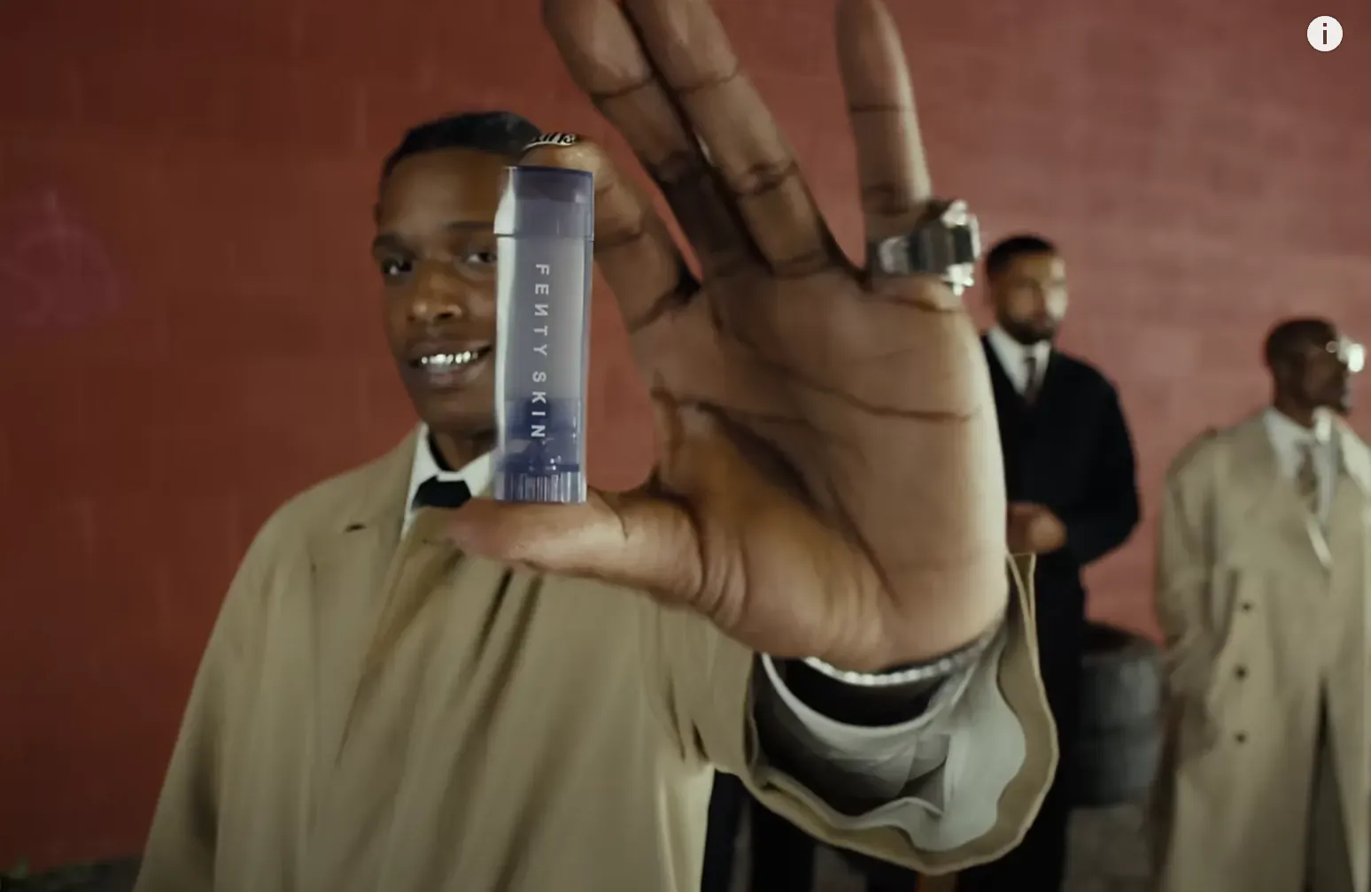 Man in a tan trench coat holding a Fenty Skin stick up toward the camera