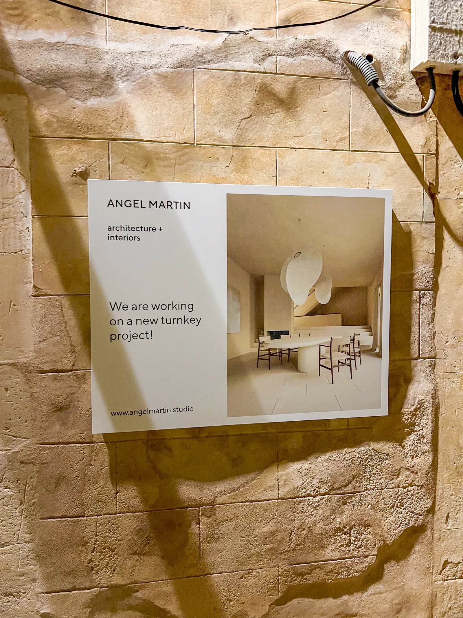 Printed sign on a limestone wall reading Angel Martin architecture and interiors with an interior render