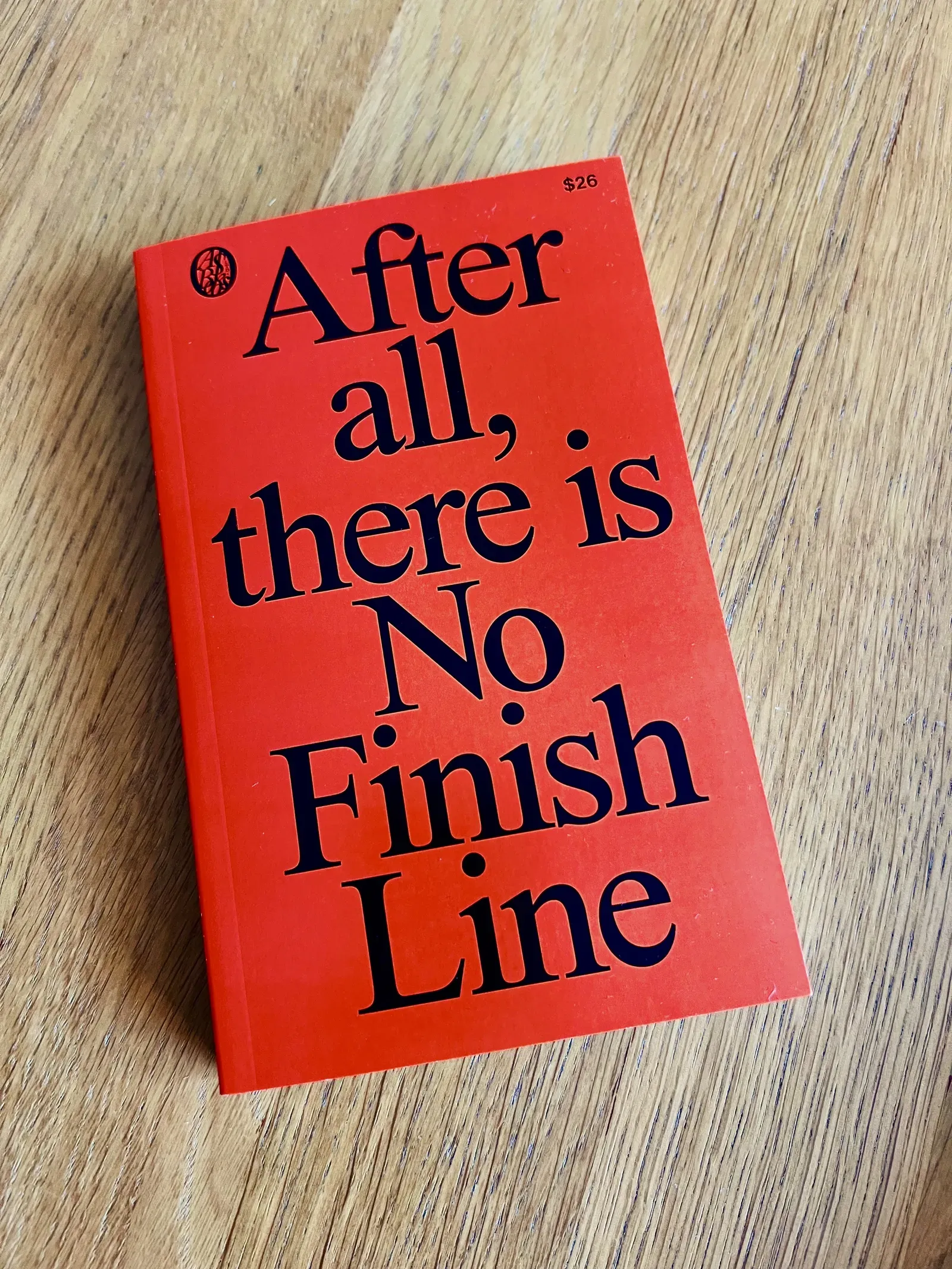 Red paperback titled After all, there is No Finish Line lying on a wooden table