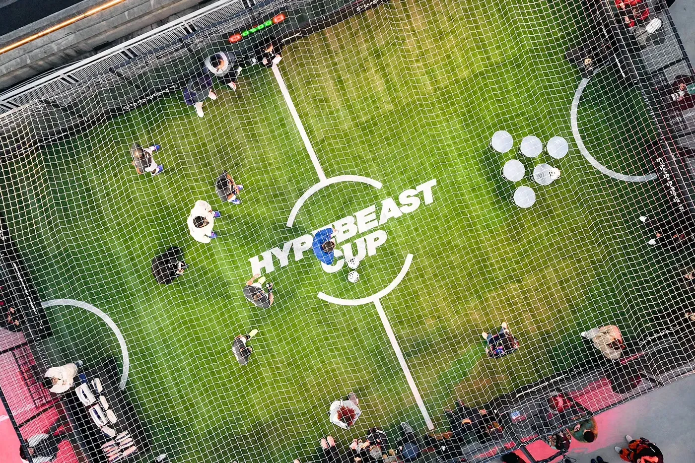 Overhead view through netting of a small green pitch marked with the HYPEBEAST CUP centre-circle logo