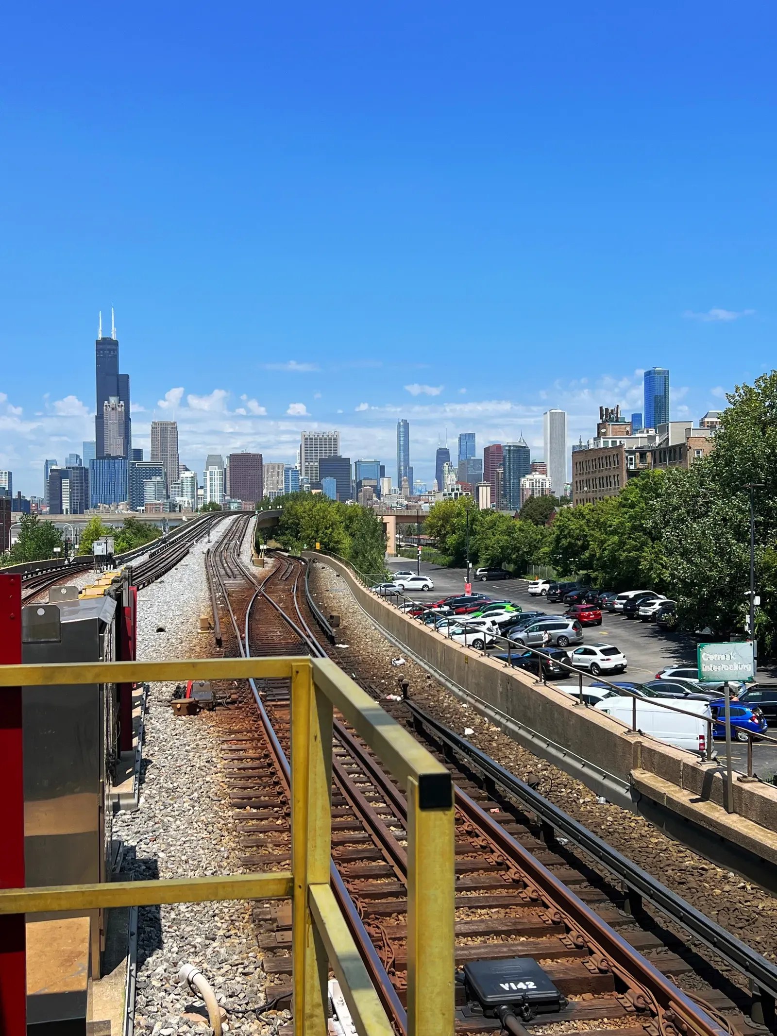 Elevated train tracks curving toward the Chicago skyline under a bright blue summer sky