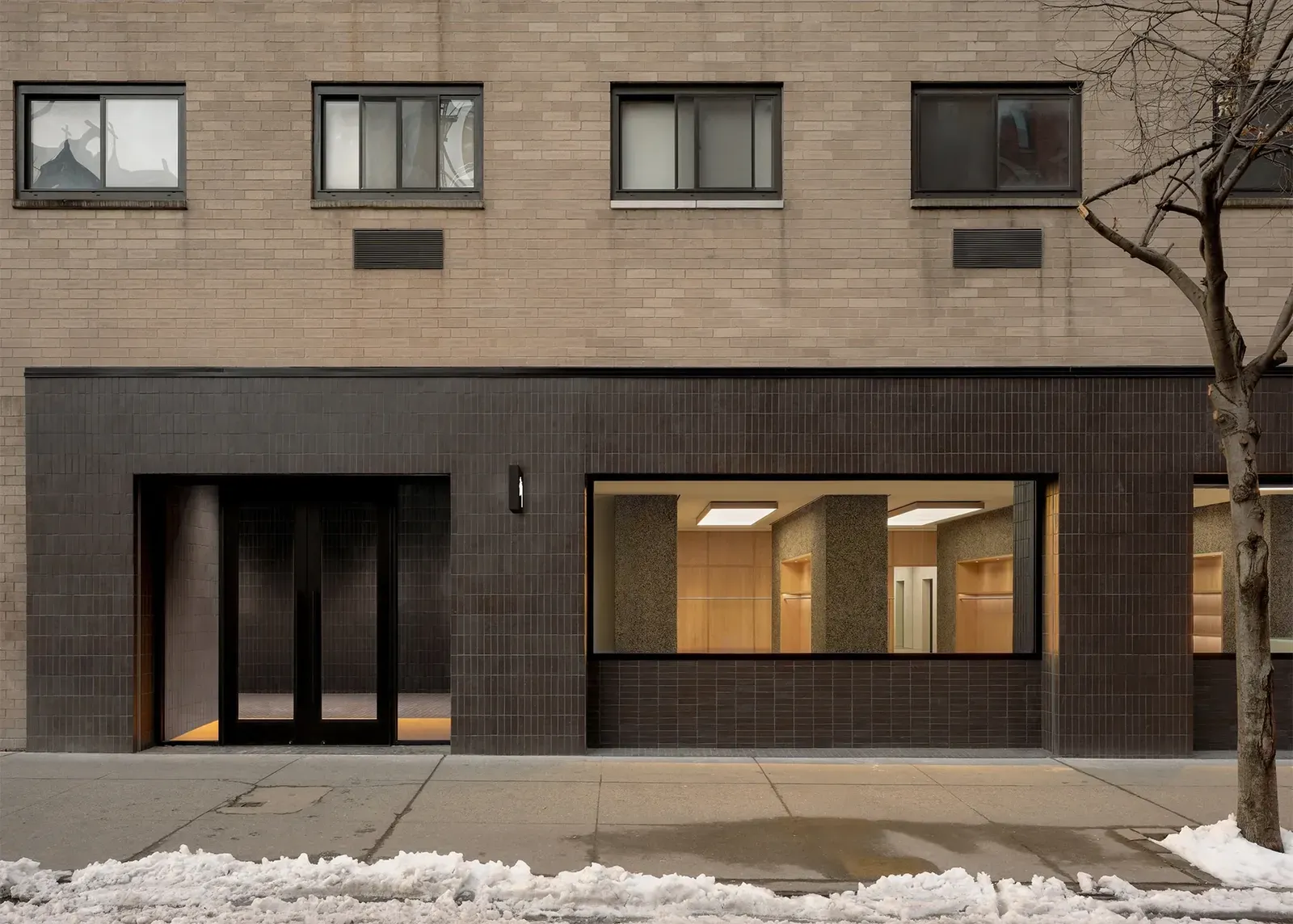 Dark brick storefront with a large lit display window and melting snow along the sidewalk
