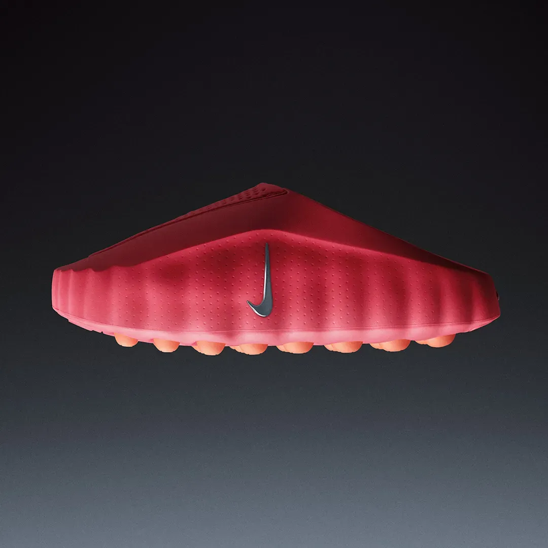 Red Nike Mind shoe in side view with a silver swoosh, a row of rounded orange foam nodes peeking out under the sole
