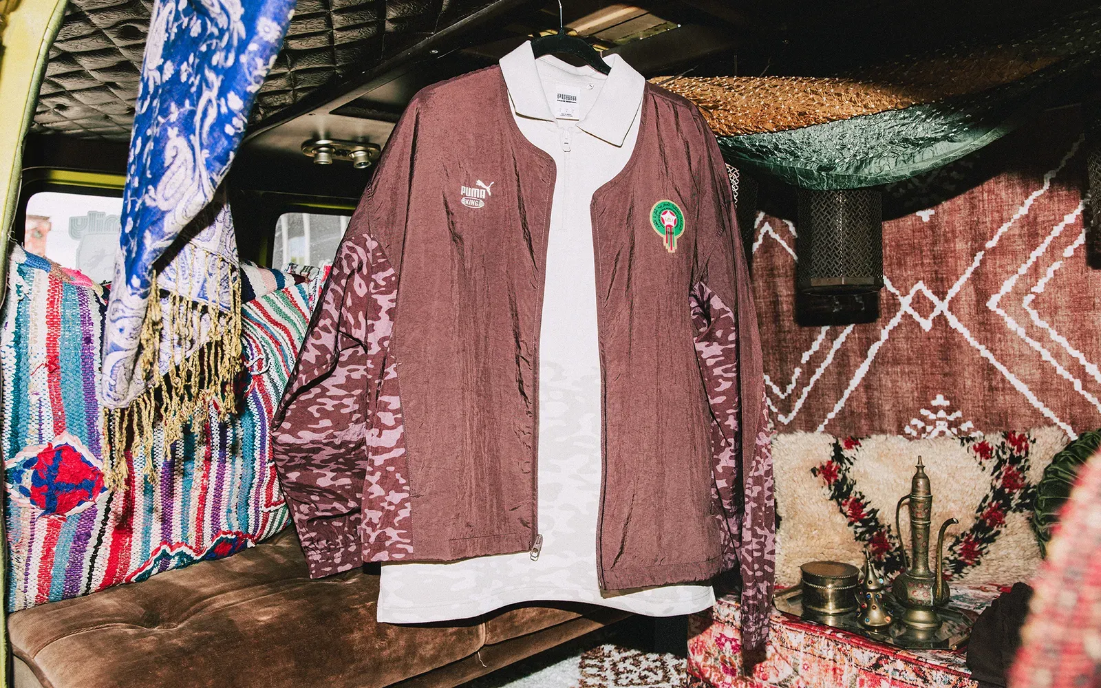 Brown Puma KING track jacket with the Morocco crest over a cream half-zip, hanging in a van lined with rugs and cushions