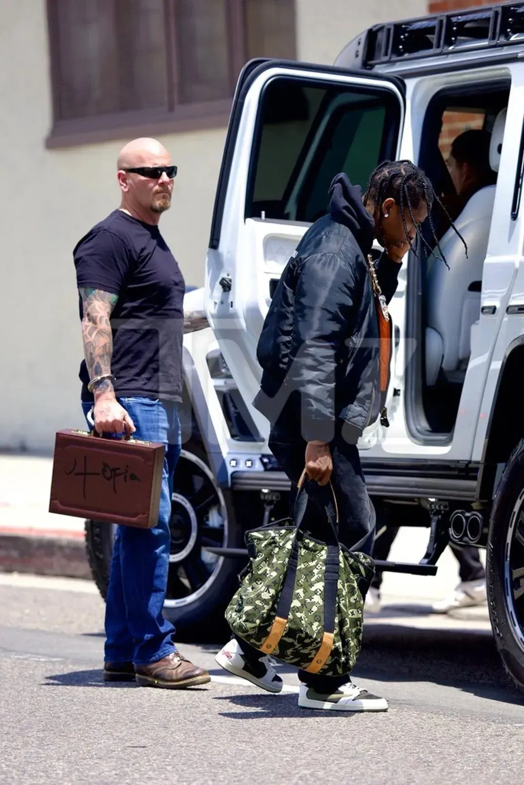 Travis Scott’s bodyguard with a brown Utopia briefcase cuffed to his wrist, as Travis steps into a white SUV