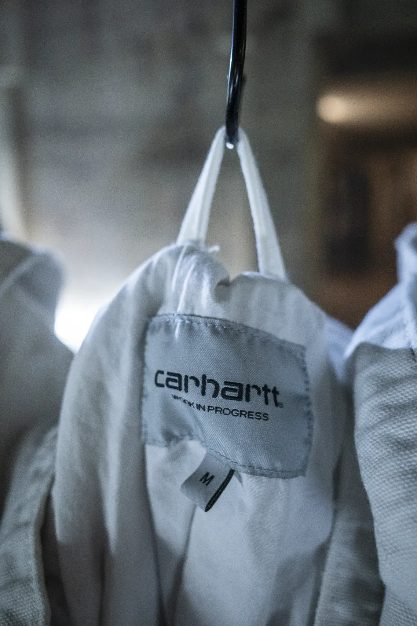 Pale jacket on a black hook, its Carhartt Work in Progress label and size M tag showing