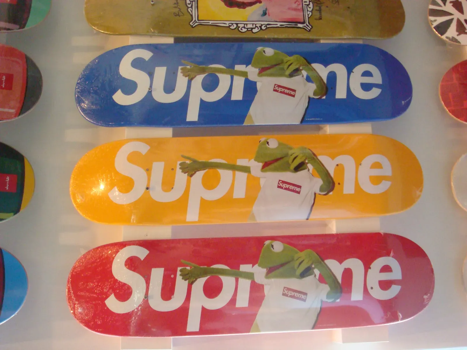 Three Supreme skate decks in blue, yellow and red, each printed with Kermit the Frog wearing a box logo tee
