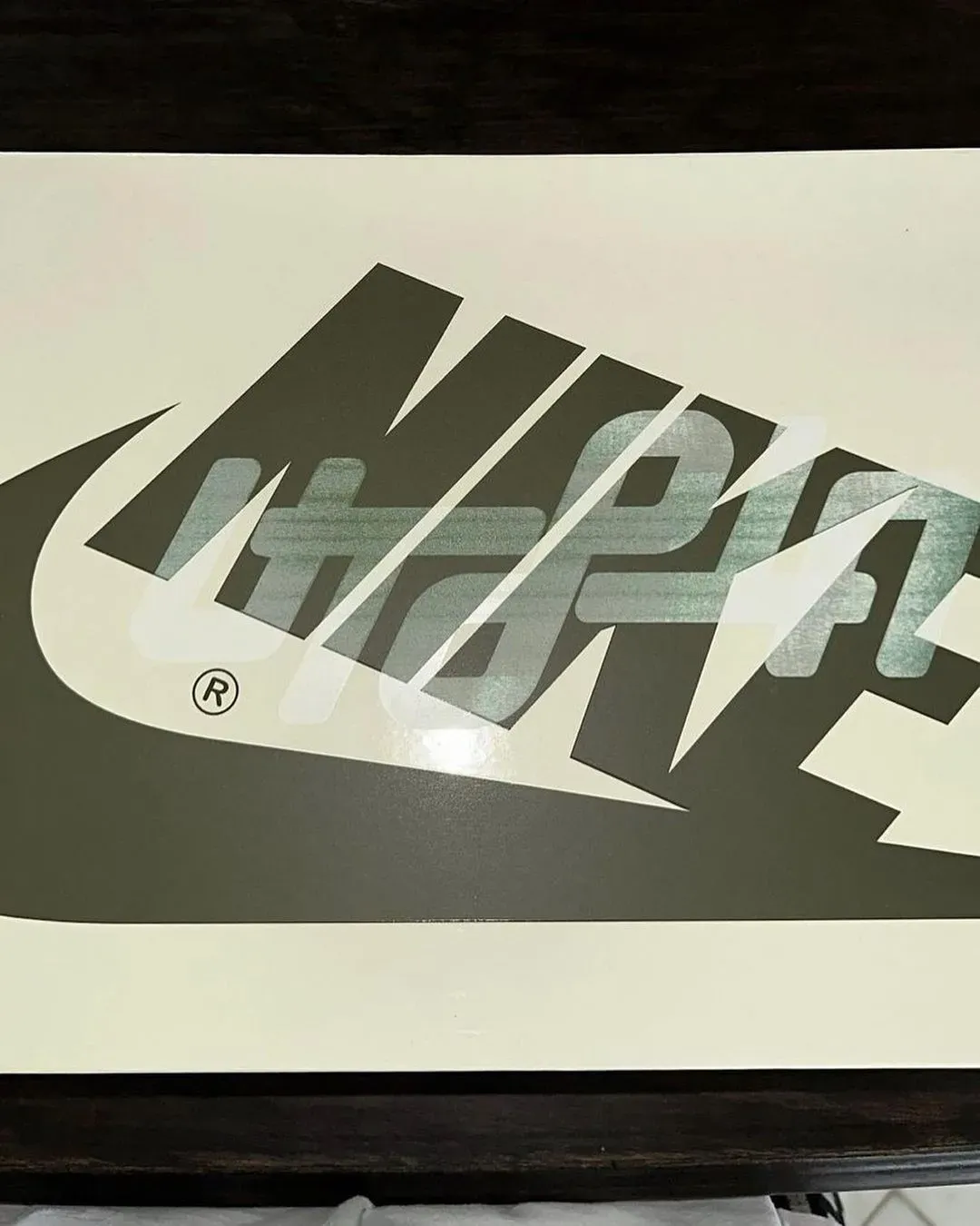Shoebox lid with a big olive Nike logo and a shiny Utopia logo printed over it