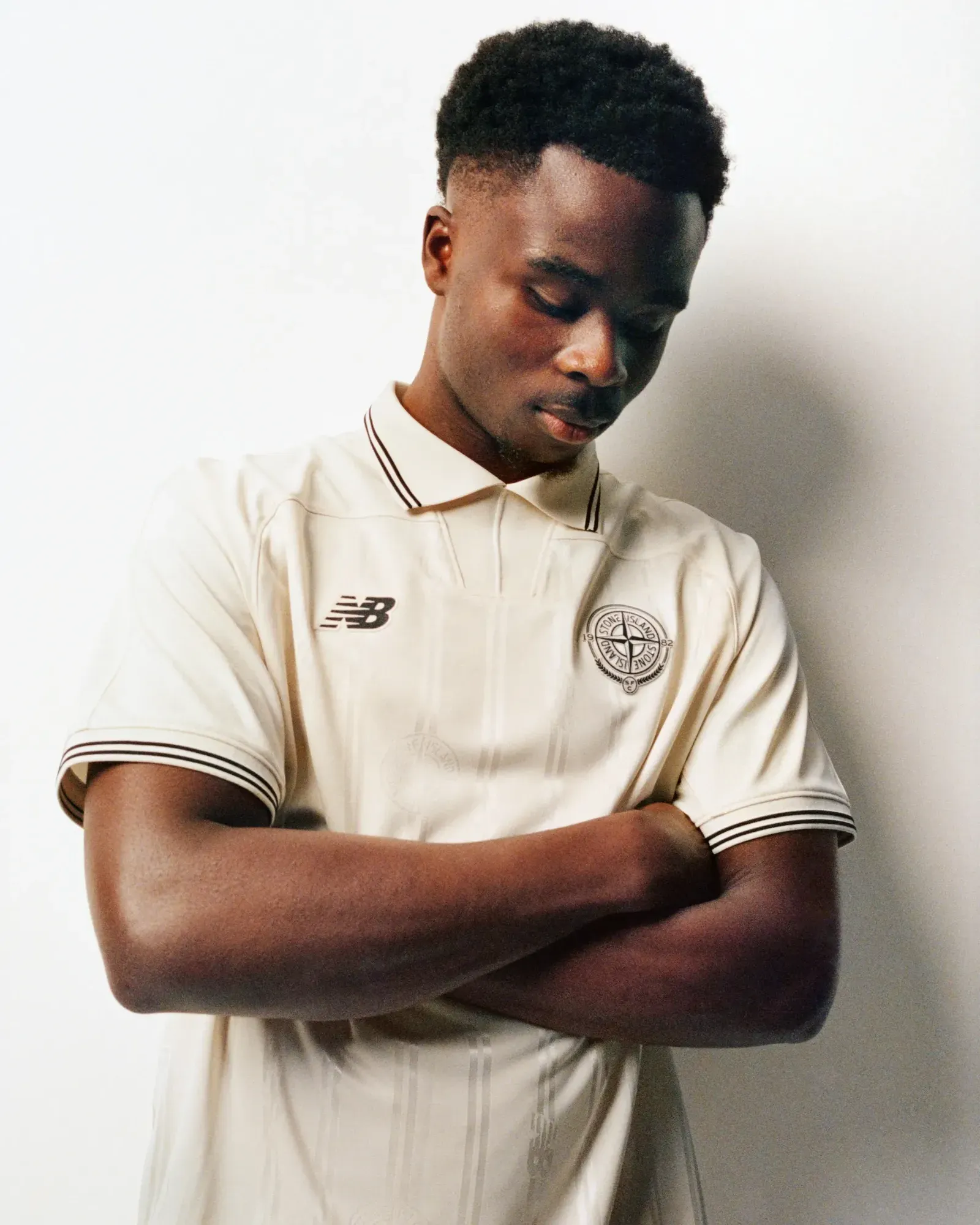 Man with folded arms in the cream New Balance x Stone Island football shirt with tipped collar and compass badge