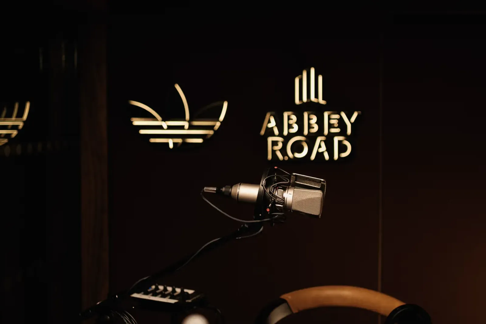 Condenser microphone in a shock mount in front of glowing adidas trefoil and Abbey Road logos on a dark wall