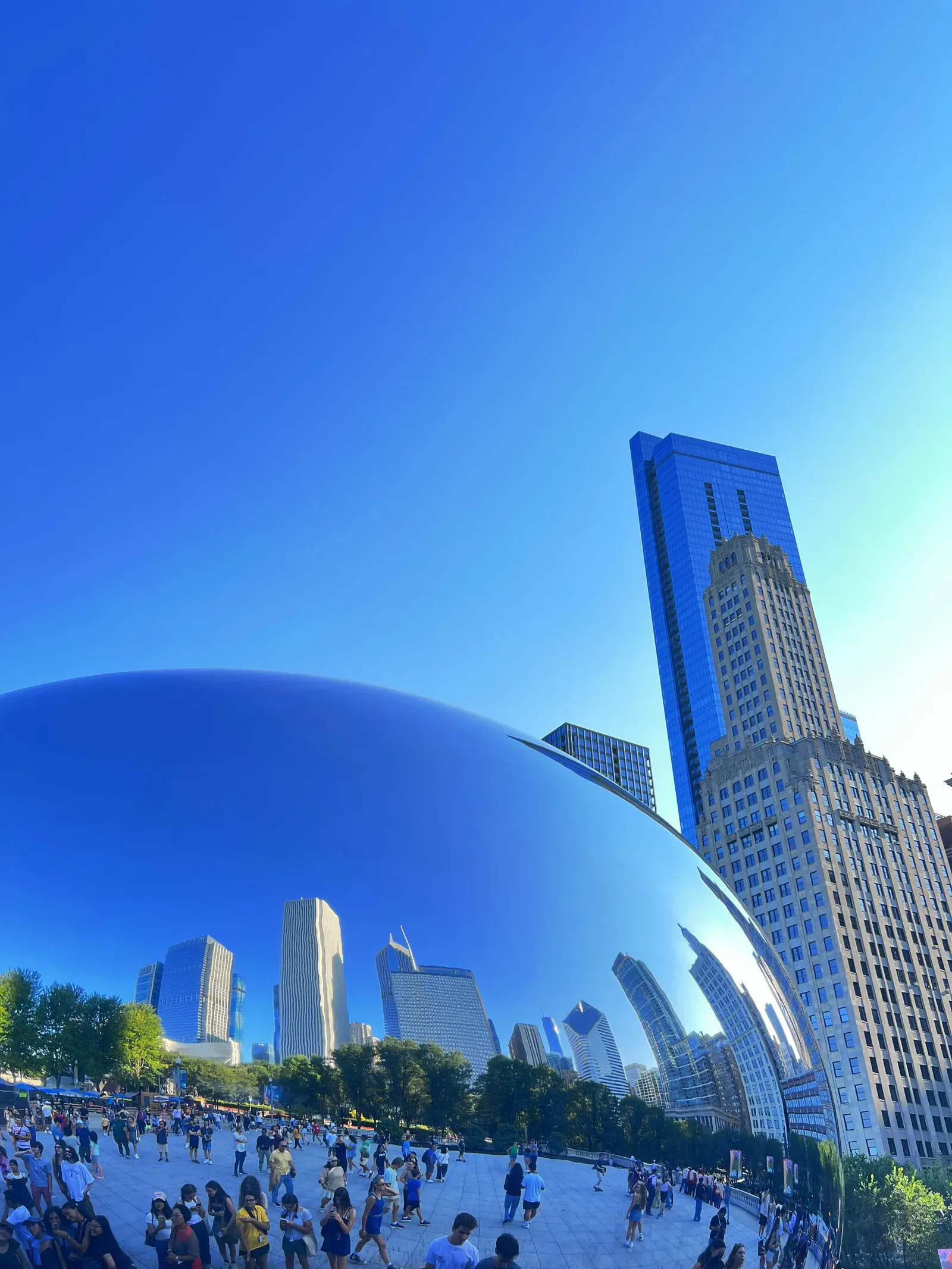 Mirrored bean-shaped sculpture reflecting the Chicago skyline and crowds of visitors under a deep blue sky