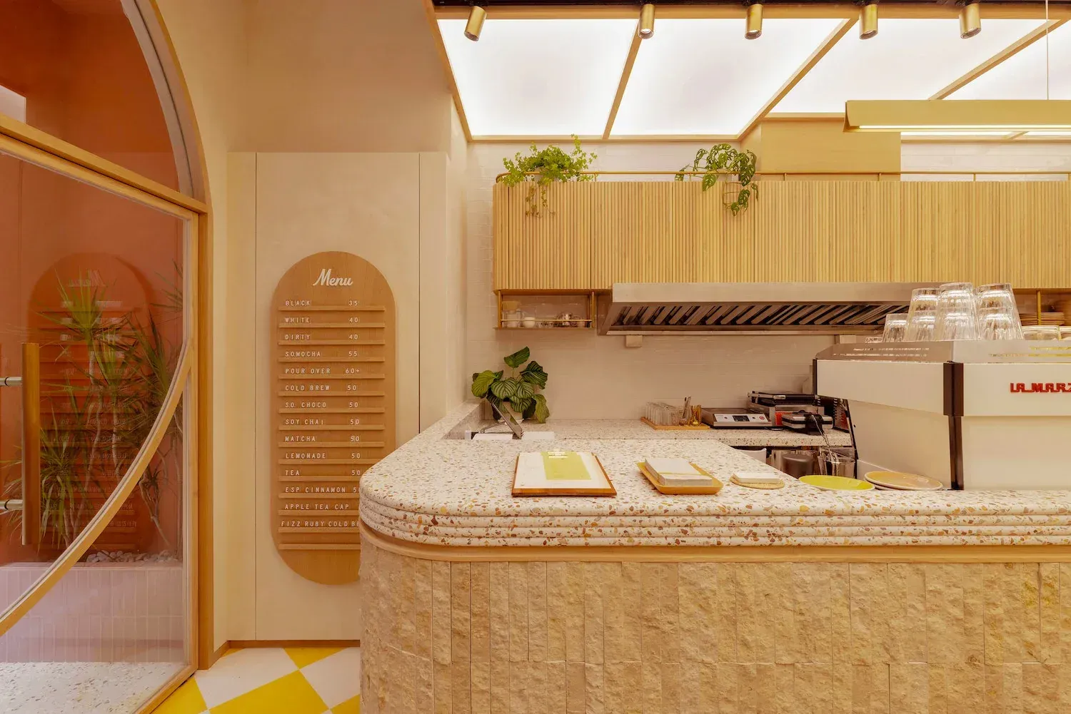 Café counter with a terrazzo top and stone base, an arched wooden menu board and an espresso machine