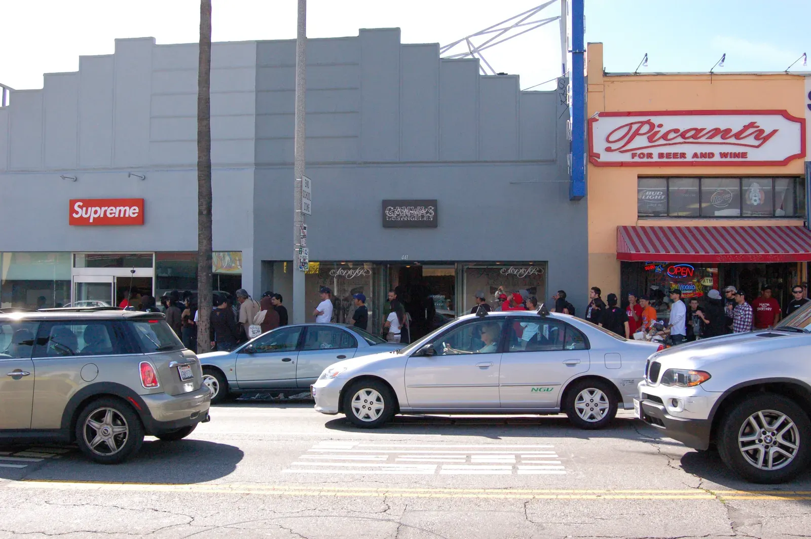 Supreme’s grey storefront seen from across the street, the line running along the sidewalk past the neighbouring shops