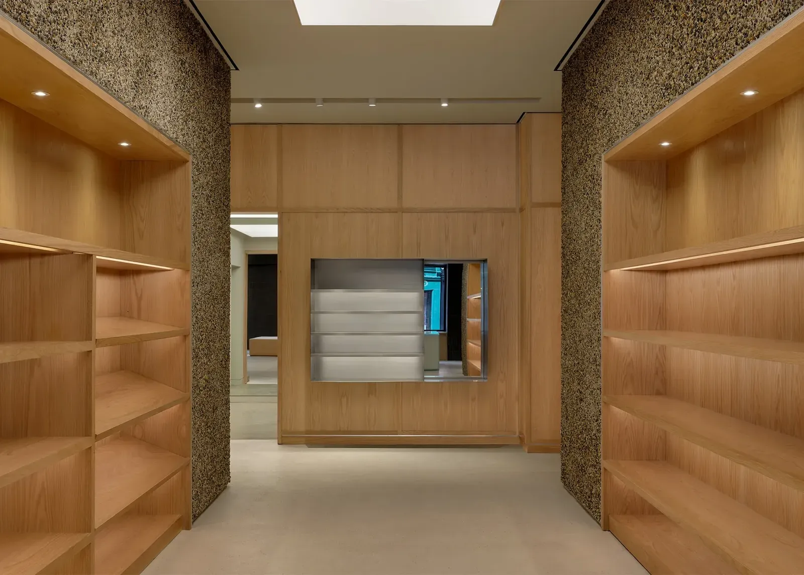 Empty oak shelves set into pebble-clad walls, facing an oak-panelled wall with a brushed steel display box