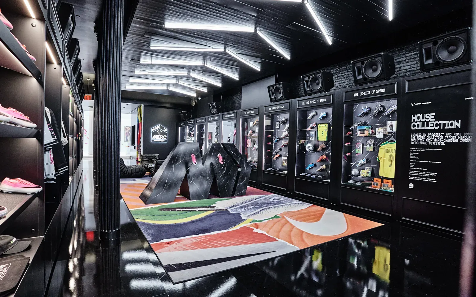 Inside House of Merc: a giant black marble M on a Nike swoosh rug, with glass cases of Mercurial boots and shirts