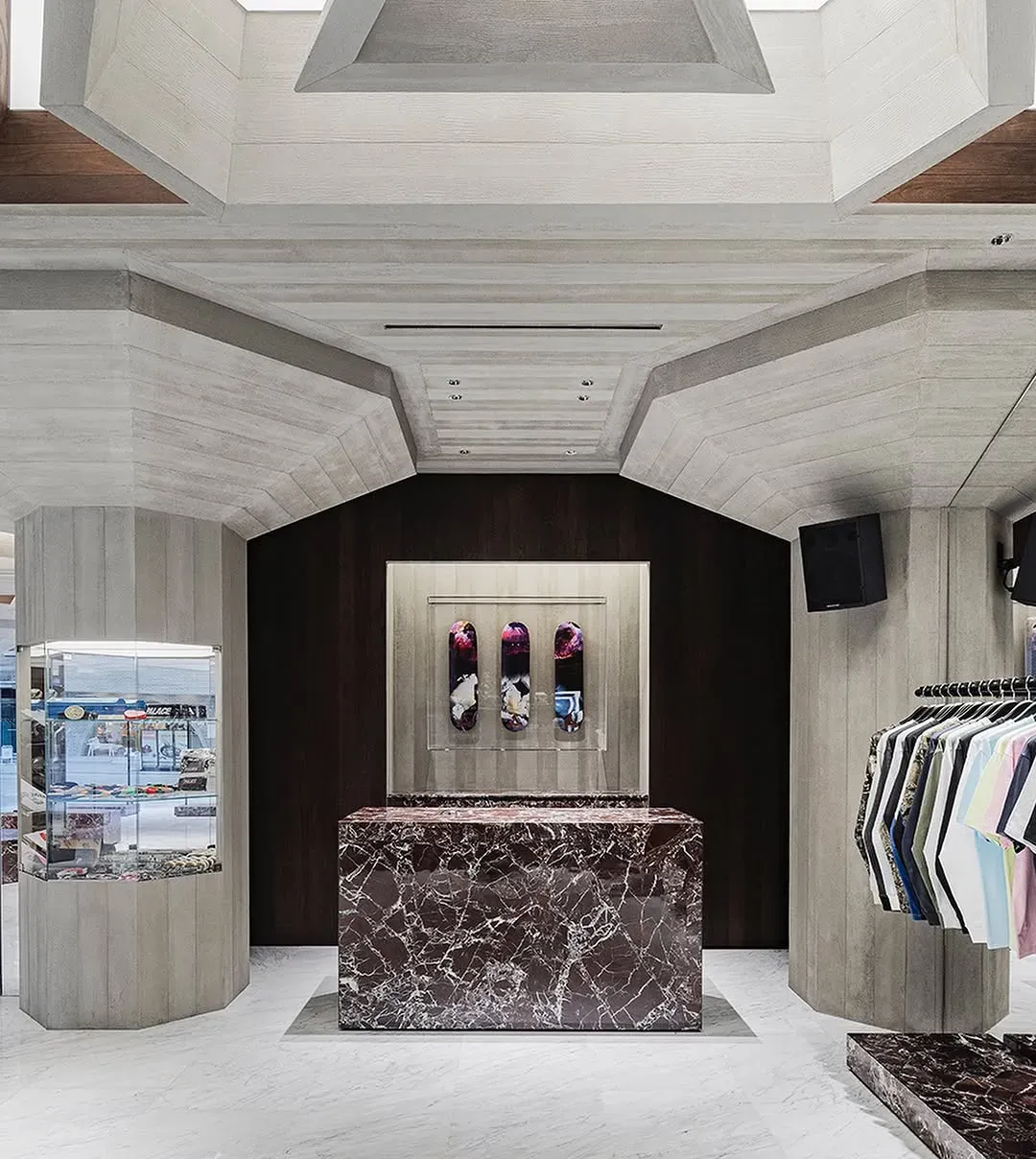 Red marble counter in front of three skateboard decks framed on a dark wood wall, a glass case and clothing rail beside it
