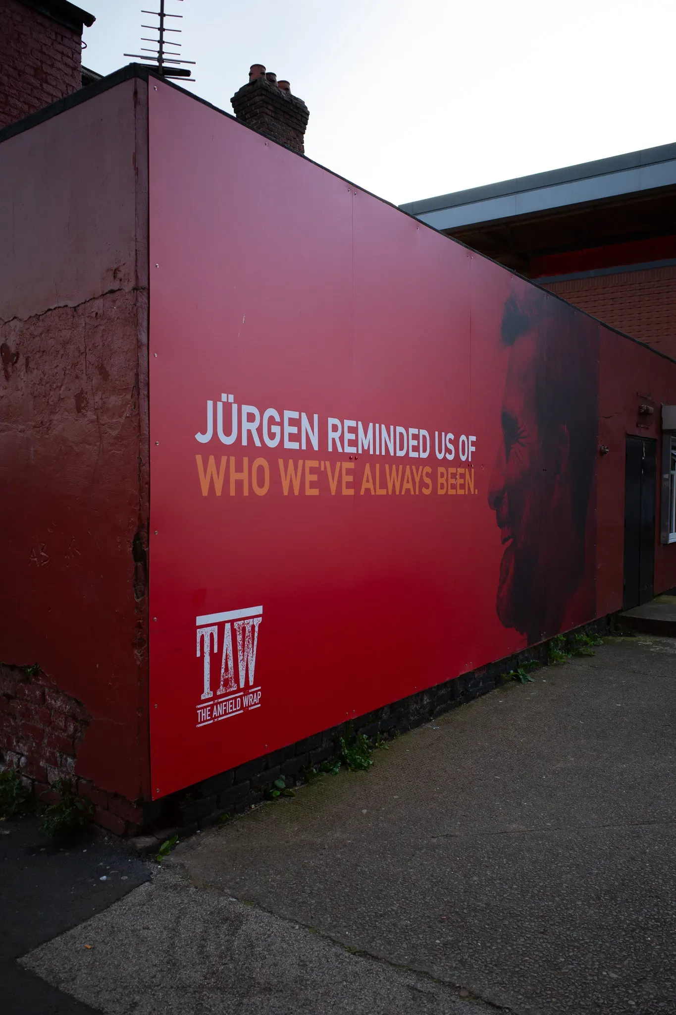 Red Anfield Wrap board on a house wall: a face in profile and the line Jürgen reminded us of who we’ve always been