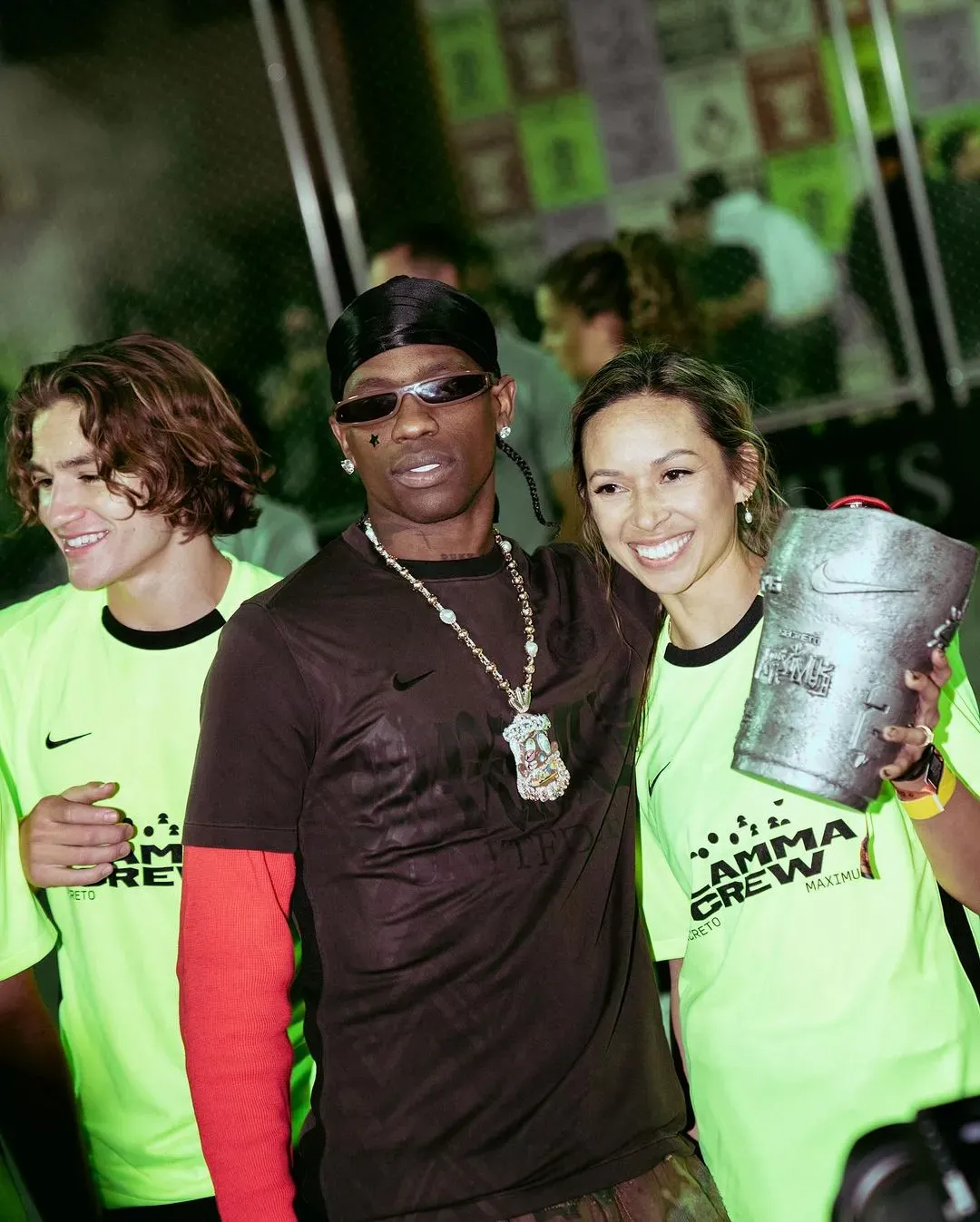 Man in durag and sunglasses poses with two smiling Flamma Crew players, one holding the silver Secreto Maximus trophy