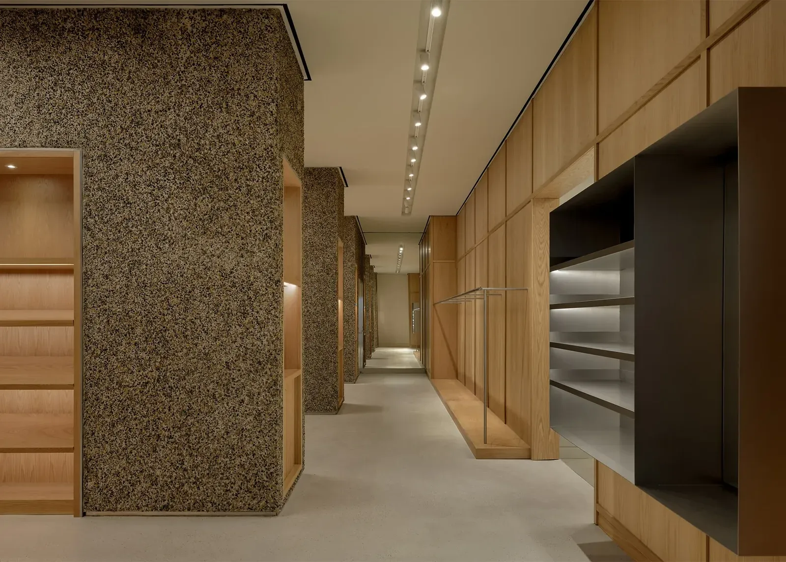 Long view between pebble-clad pillars with oak shelving and an oak-panelled wall with a steel rail and dark shelf box