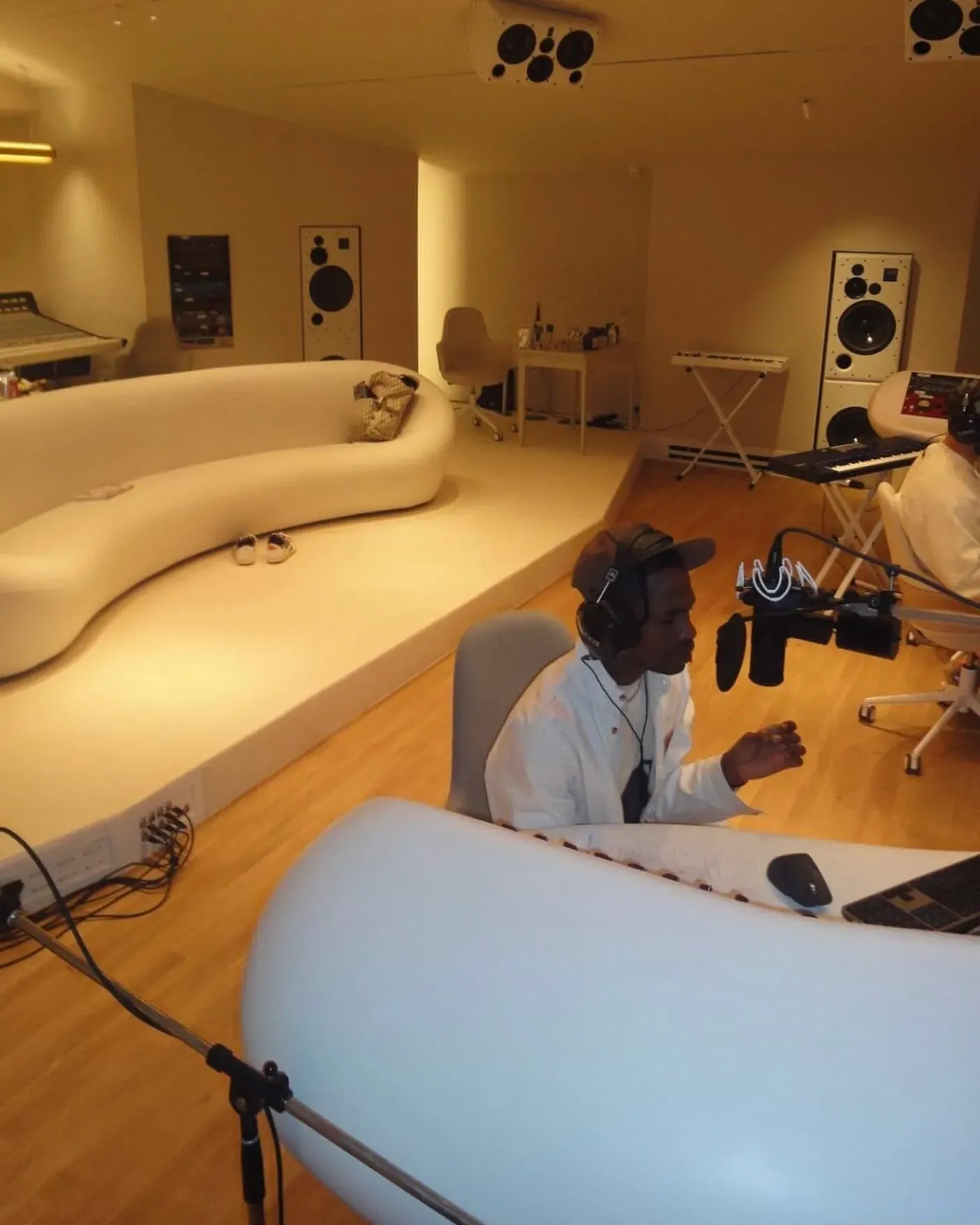 Travis Scott in headphones recording at a microphone in Miraval Studio, a curved white sofa and big speakers behind