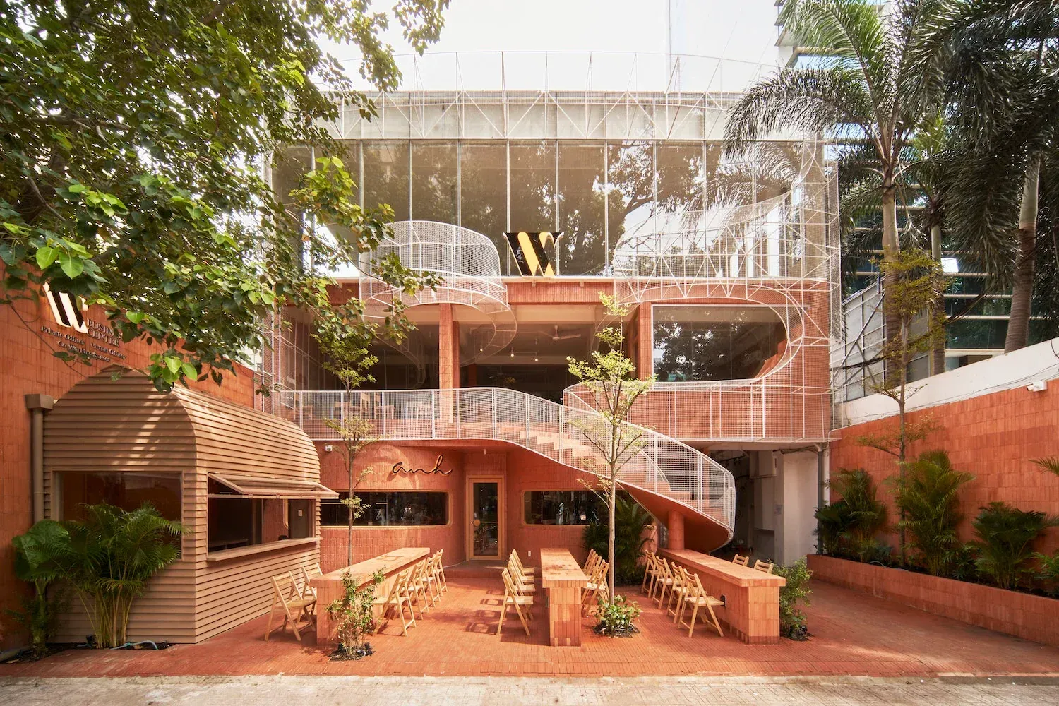 Café courtyard with brick tables and folding chairs in front of a terracotta building with a white mesh spiral staircase