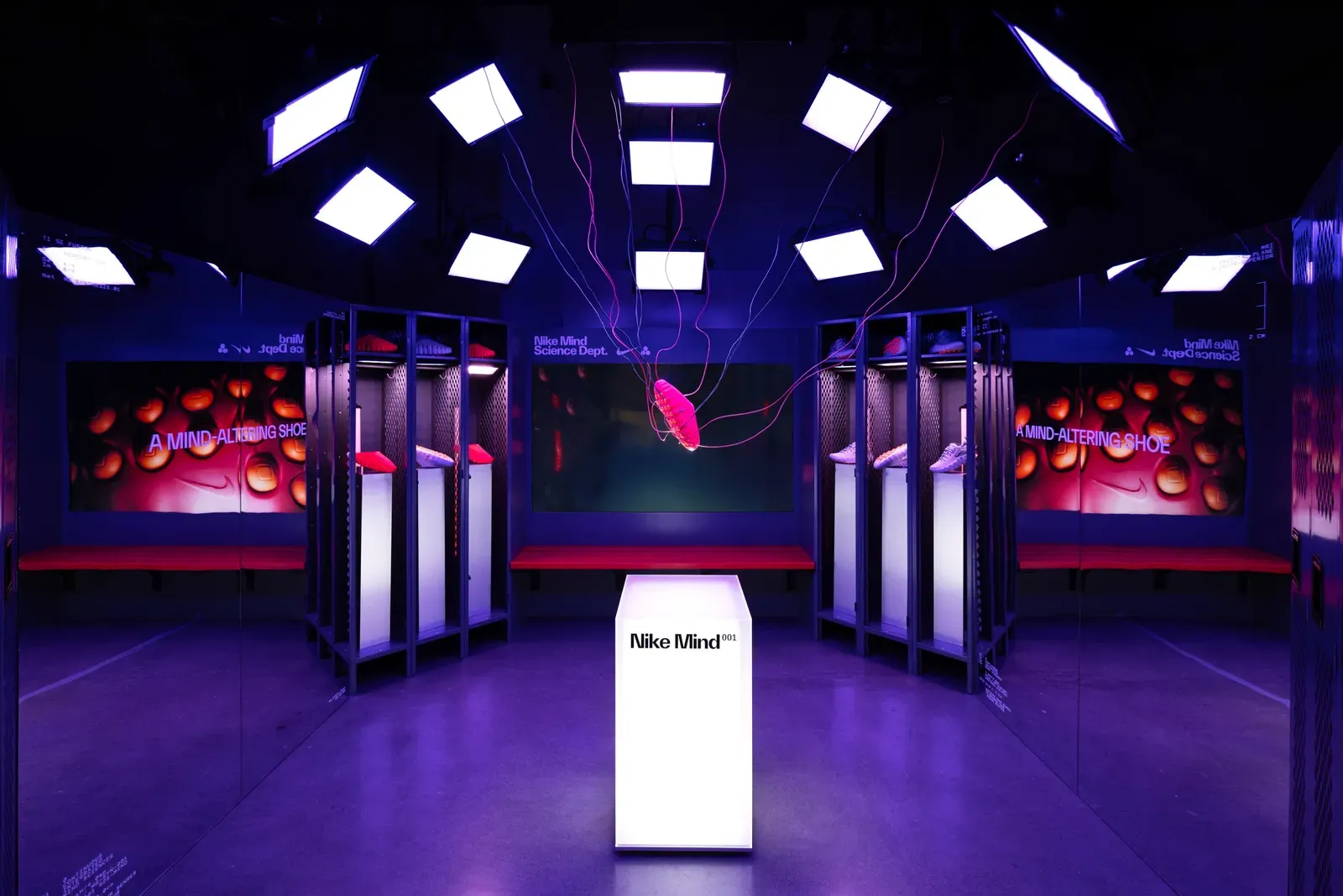Purple-lit Nike Mind installation styled as a locker room, a red shoe hanging on wires above a Nike Mind 001 plinth