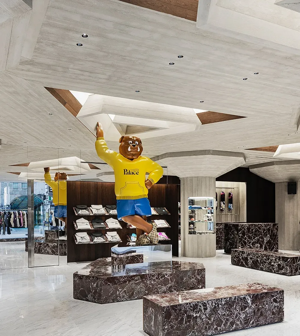 Giant bulldog figure in a yellow Palace hoodie reaching up to the ceiling over red marble benches and T-shirt shelves