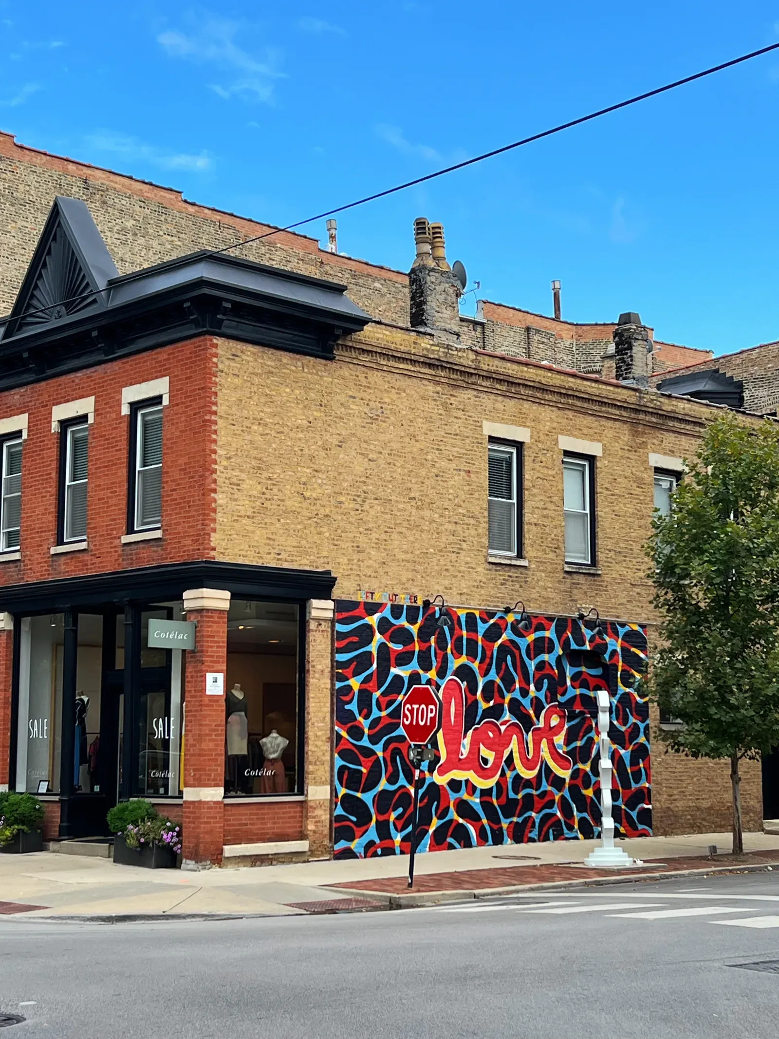 Brick corner building with a Cotélac boutique and a colourful mural reading love next to a stop sign