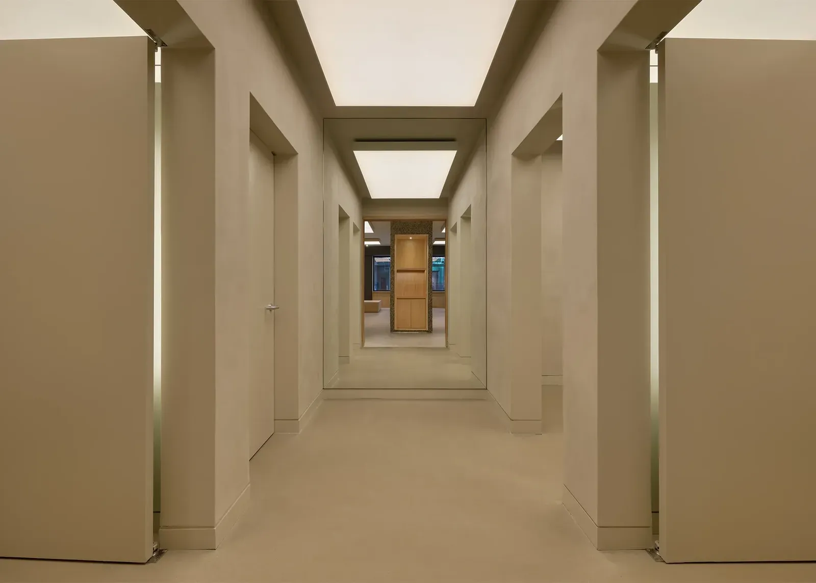 Pale beige fitting-room corridor with tall doors swung open and a mirror at the end reflecting the shop floor