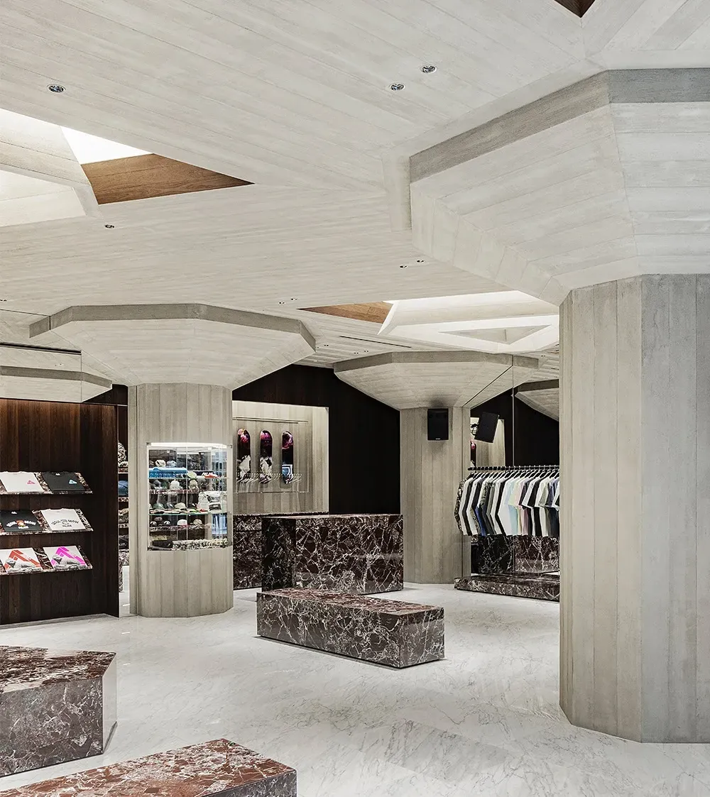 Shop floor with octagonal wood-grain concrete pillars, red marble benches, a glass case of caps and a rail of shirts