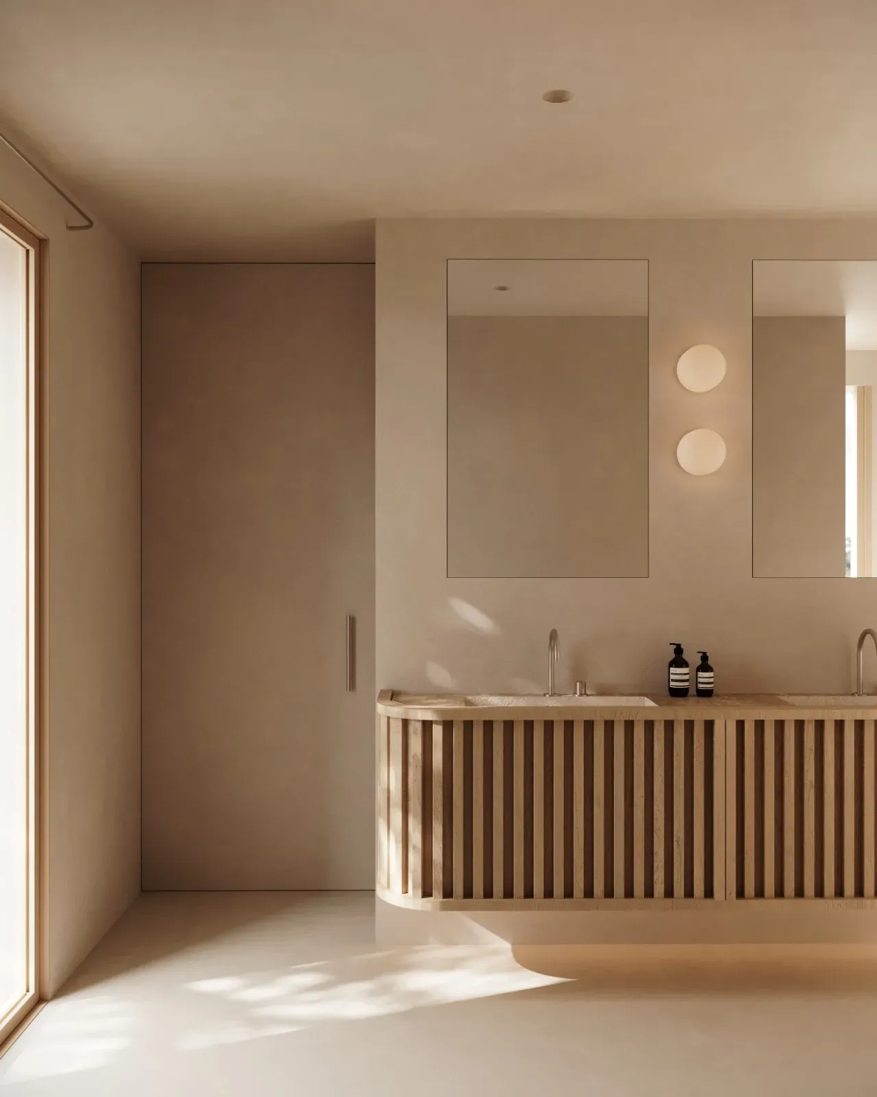 Bathroom with a curved, slatted oak double vanity, frameless mirrors, round wall lights and sunlight on a pale floor