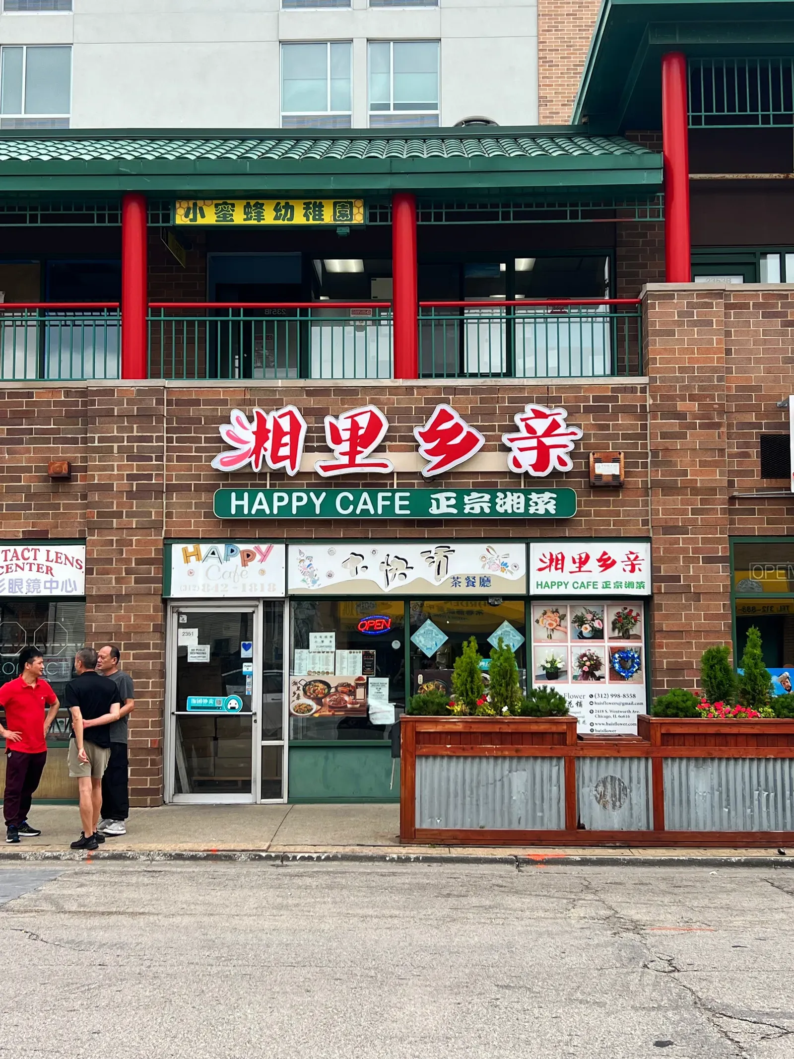 Happy Cafe with Chinese signs, red pillars and a green tiled roof above, three men chatting on the street outside