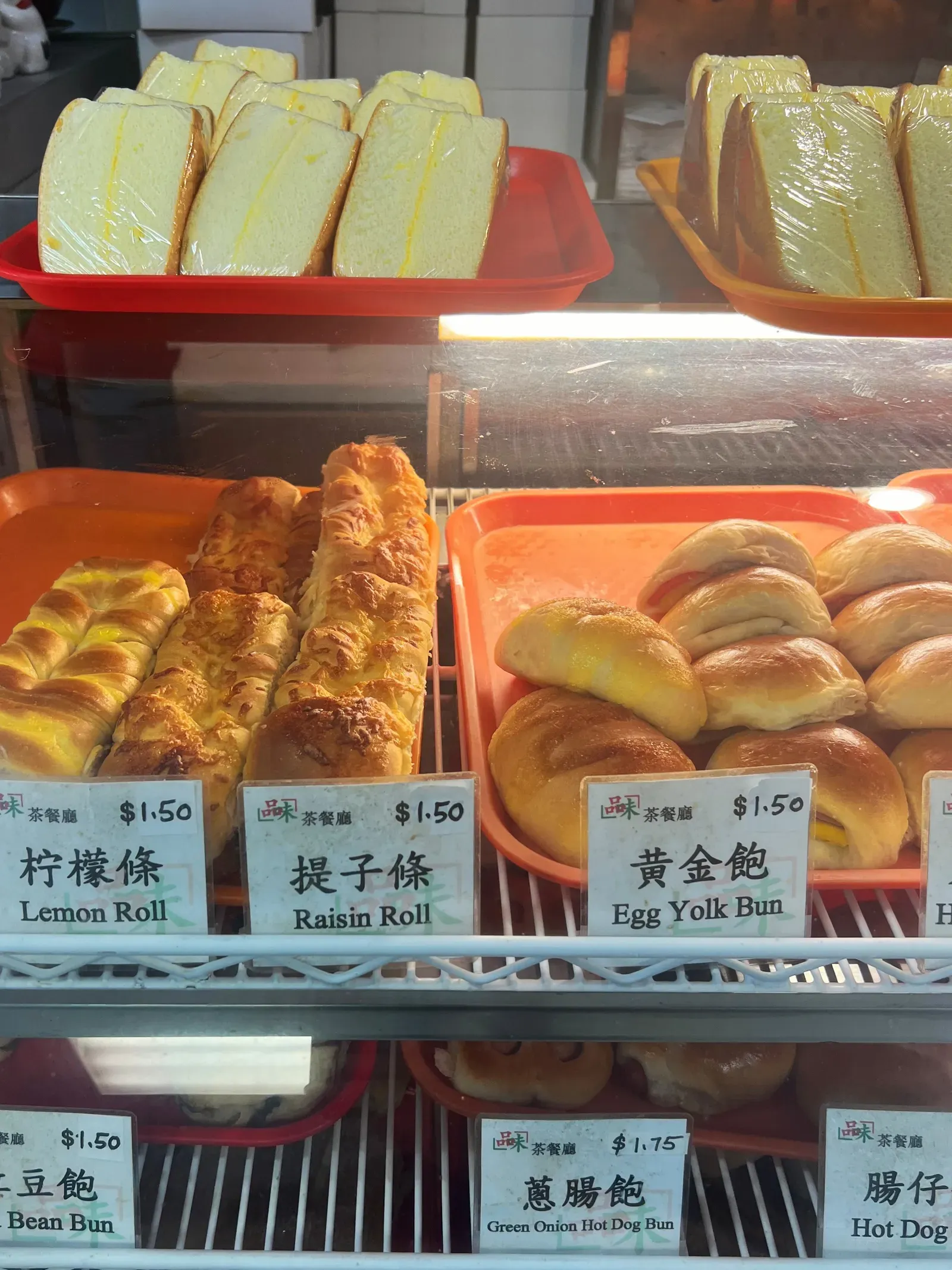 Bakery case with lemon rolls, raisin rolls and egg yolk buns at $1.50 each, labelled in Chinese and English