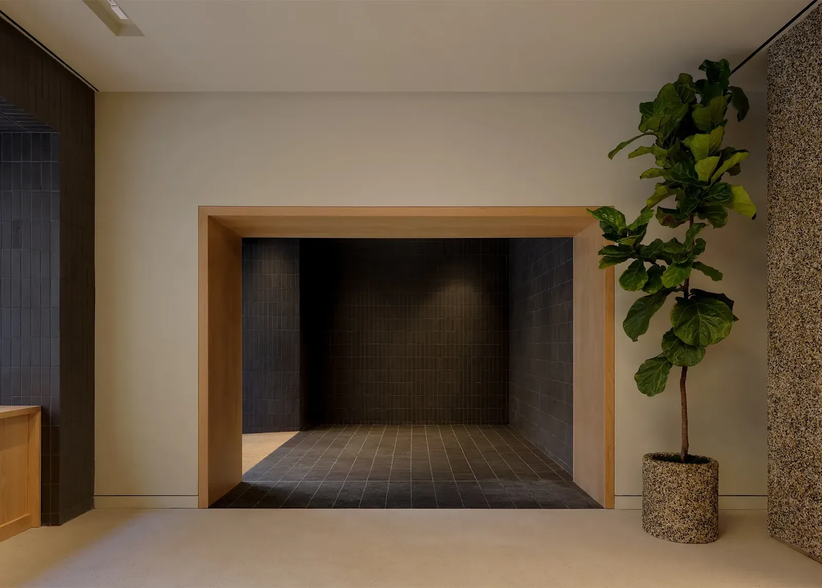 Recessed alcove of dark tiles framed in thick oak, beside a fiddle-leaf fig in a pebble-textured planter