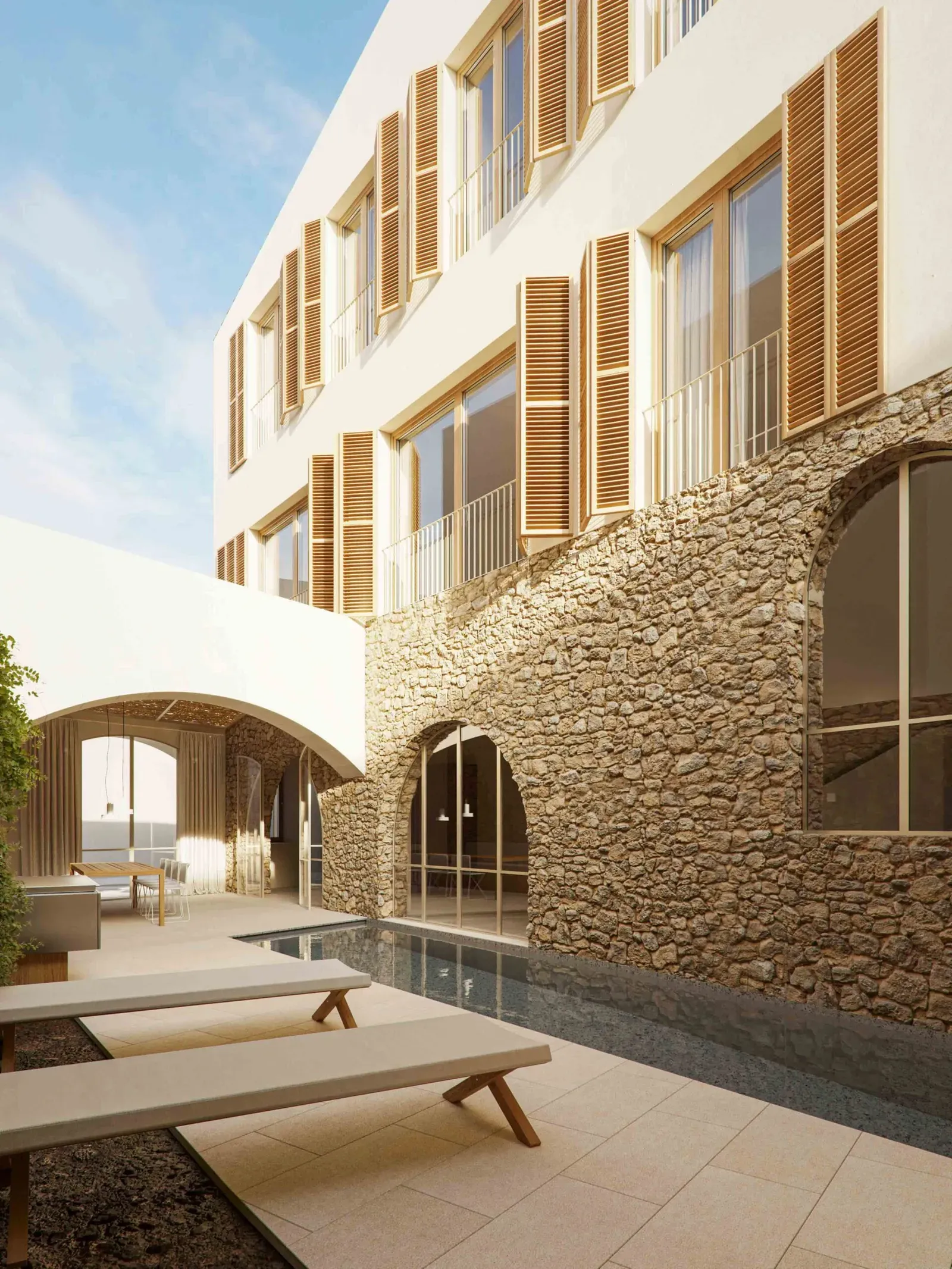 Patio with a narrow pool along an old stone wall with arched windows, white upper floors and wooden shutters