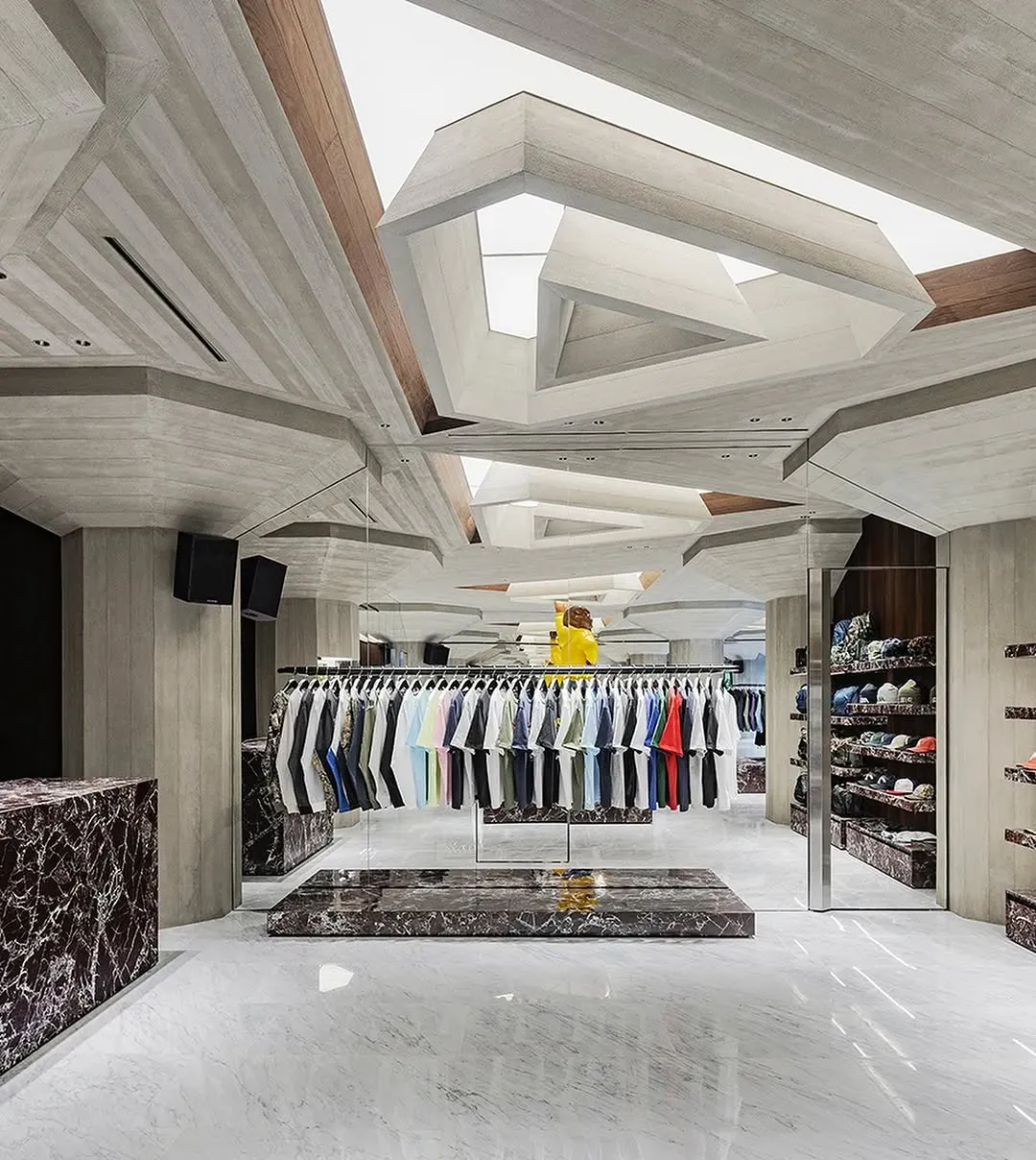 Long rail of pastel and bright T-shirts on a red marble plinth under the angular concrete ceiling, caps shelved at right