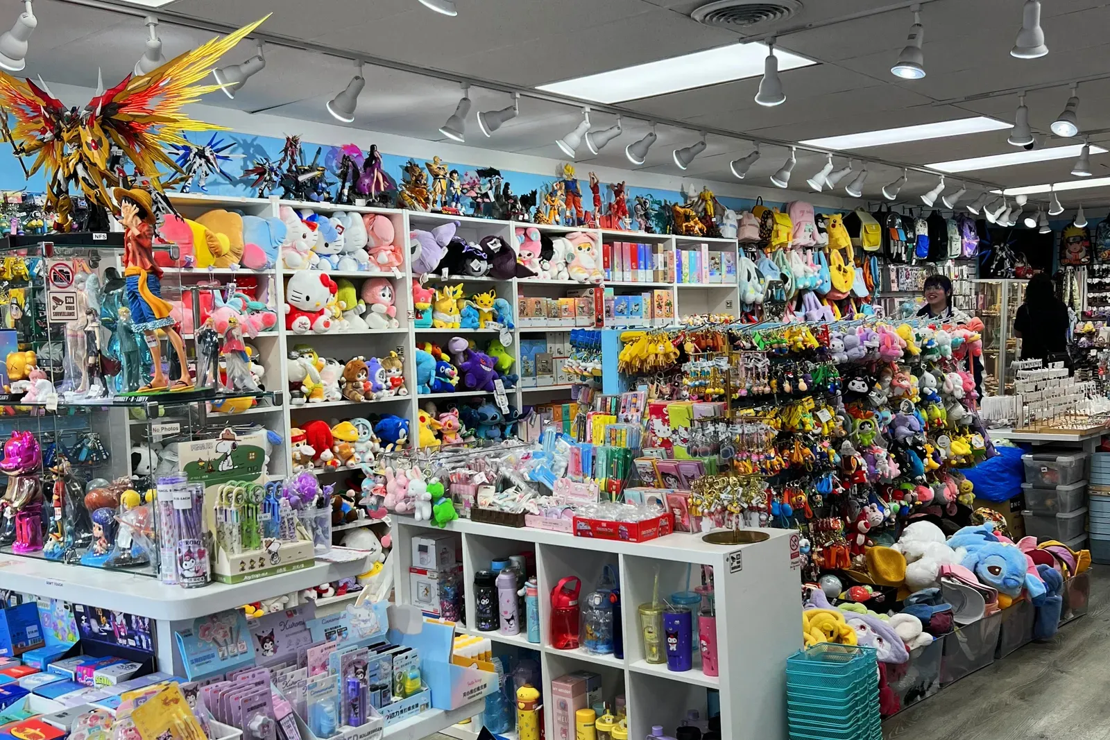 Shop crammed with anime figures, plush toys, keychains and water bottles on white shelves under track lights