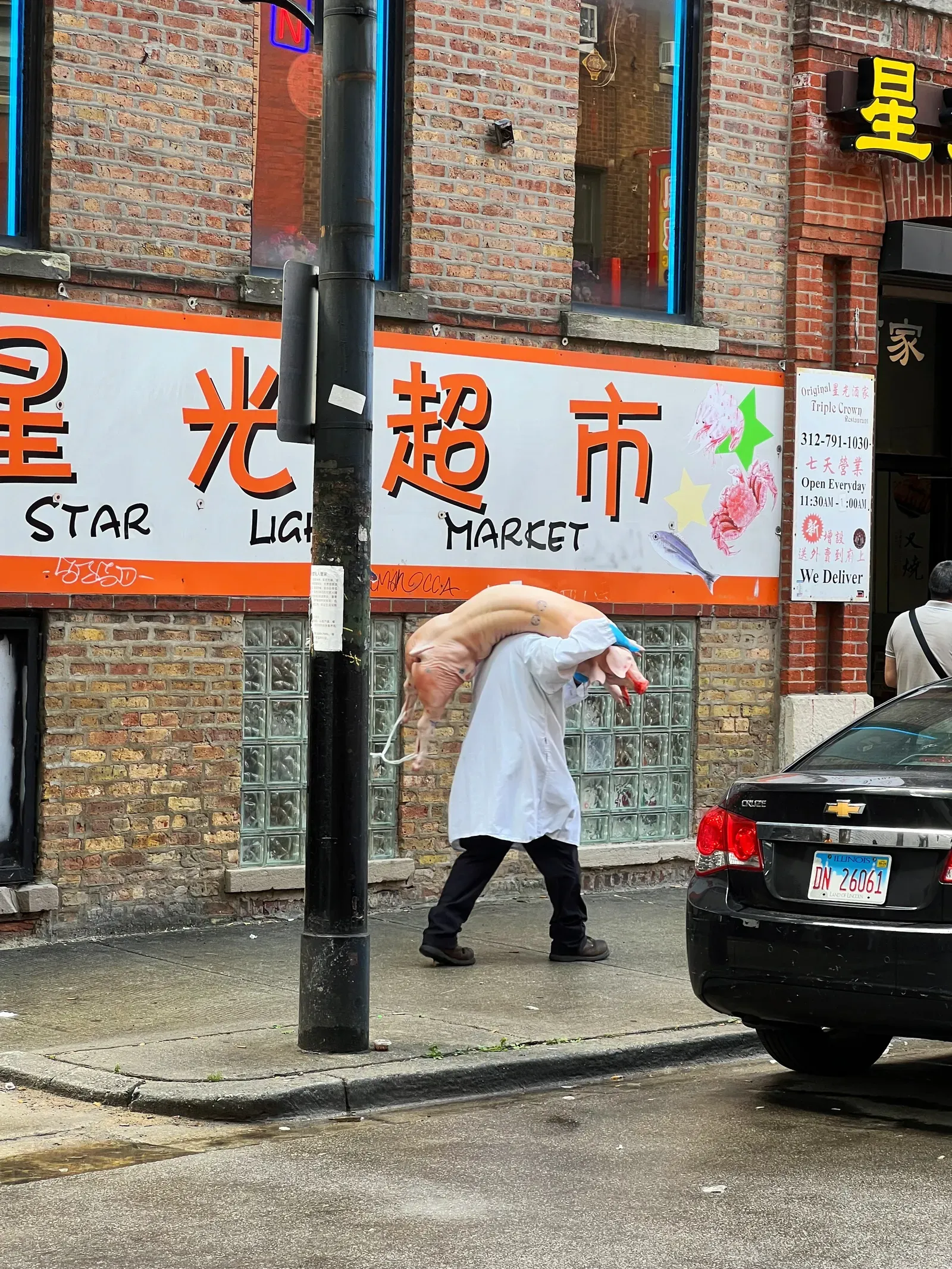 Man in a white coat carrying a whole pig over his shoulders past the Star Light Market sign in Chinese and English