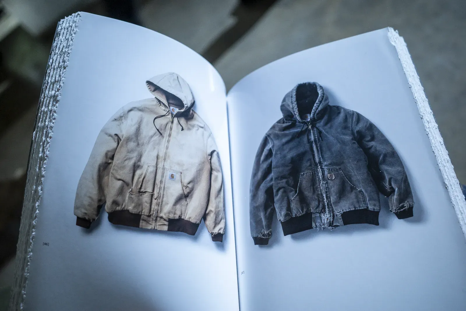 Open book spread showing two worn Carhartt hooded jackets, one tan and one faded black, frayed at the cuffs
