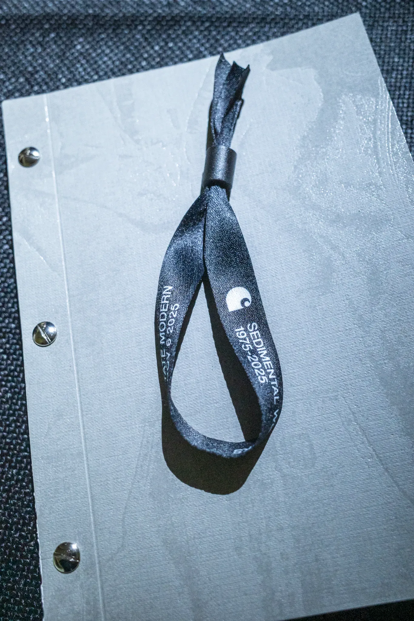 Black wristband printed with Tate Modern, Sedimental Works 1975–2025 and the Carhartt logo, on a grey cover