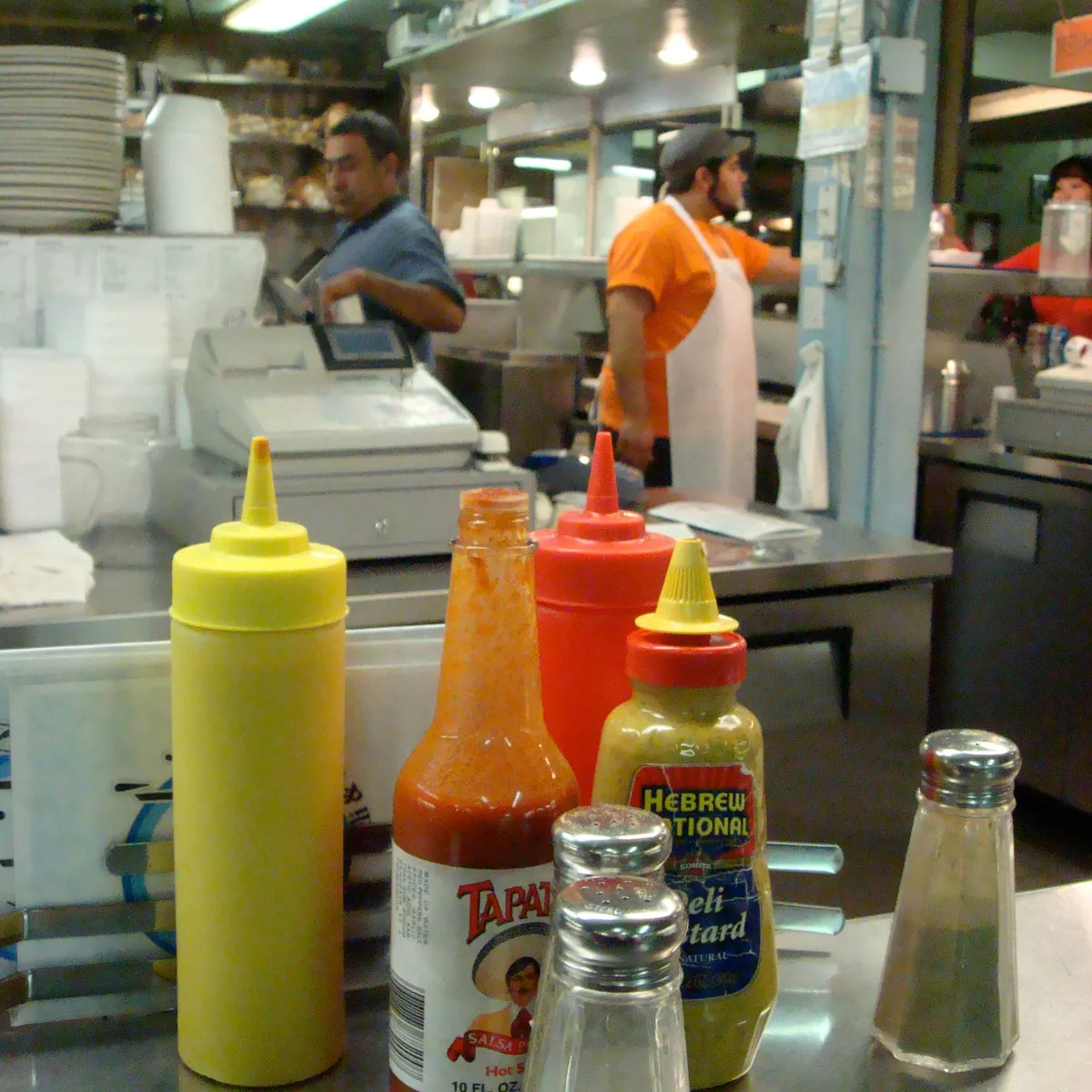 Mustard, hot sauce and salt on a diner counter, the cooks behind it.