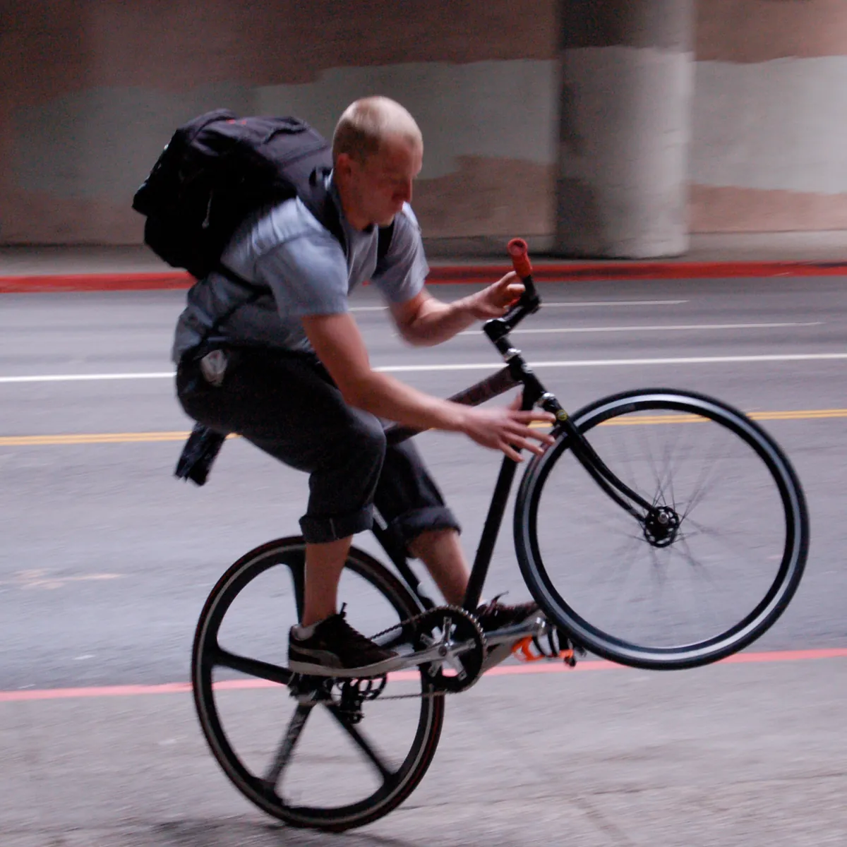 A rider pulling a wheelie on a fixed-gear bike across a Los Angeles street.