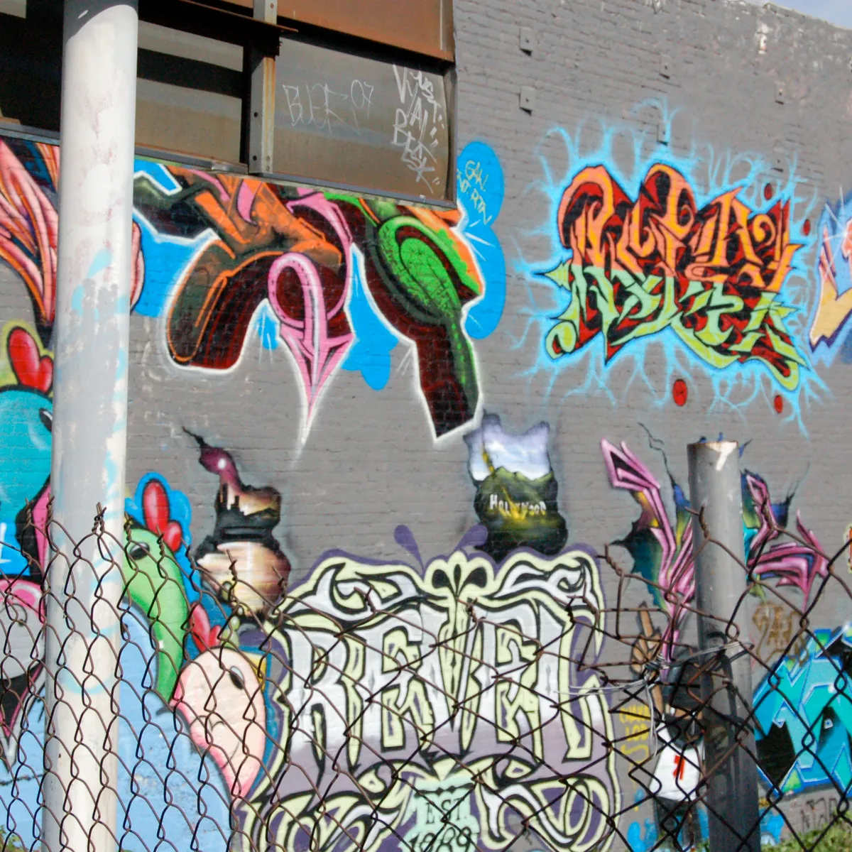 A wall covered in colourful graffiti behind a chain-link fence.