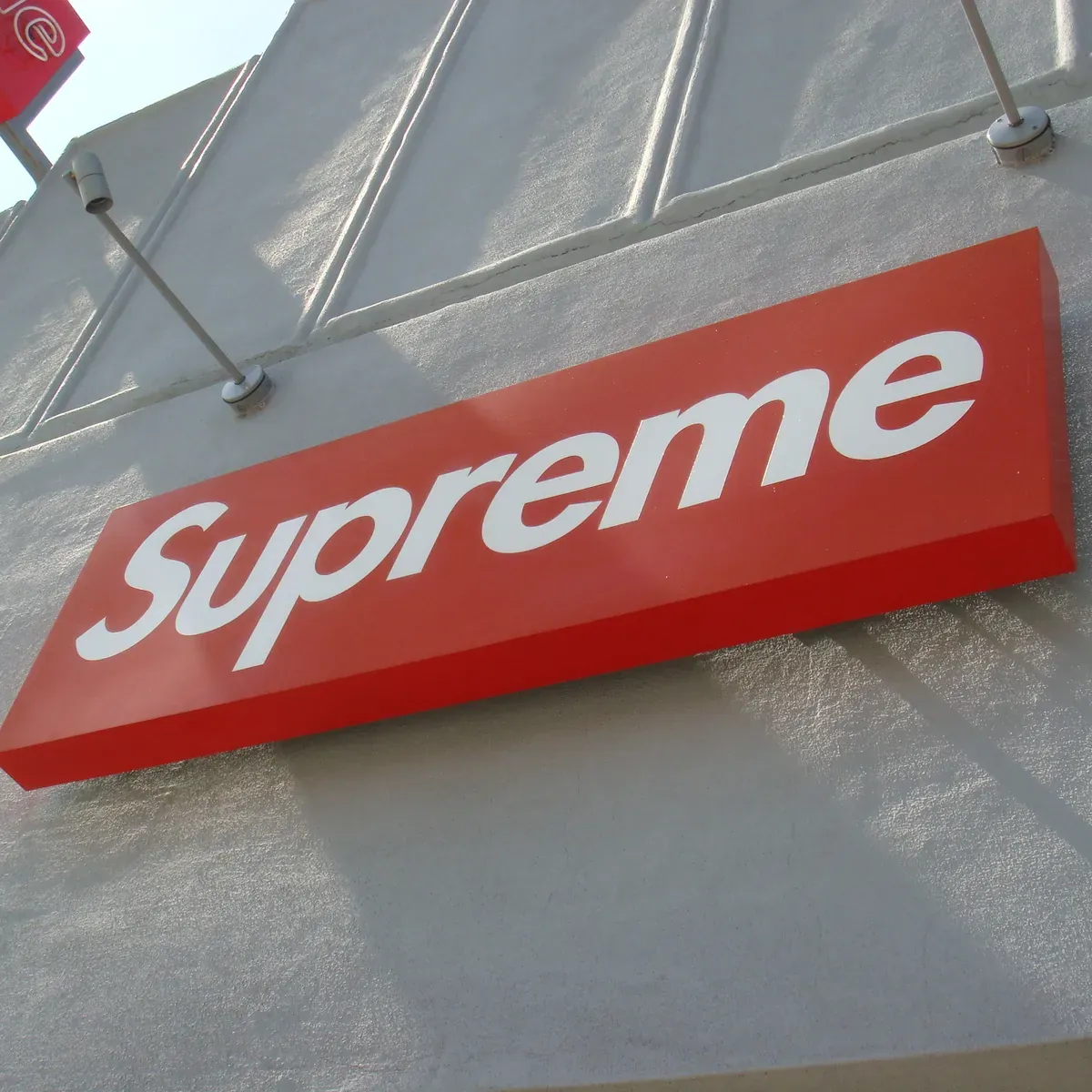 The red Supreme sign on the store front, seen from below.